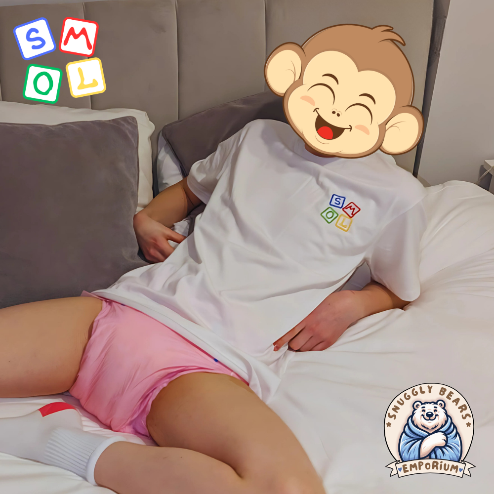 Boy wearing a white SMOL branded t-shirt and pink diper, relaxed on a bed.
