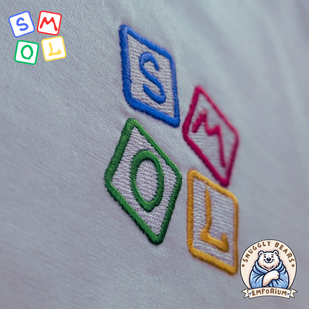 Embroidered SMOL logo in colorful blocks on a soft T-shirt fabric from Snuggly Bears Emporium.