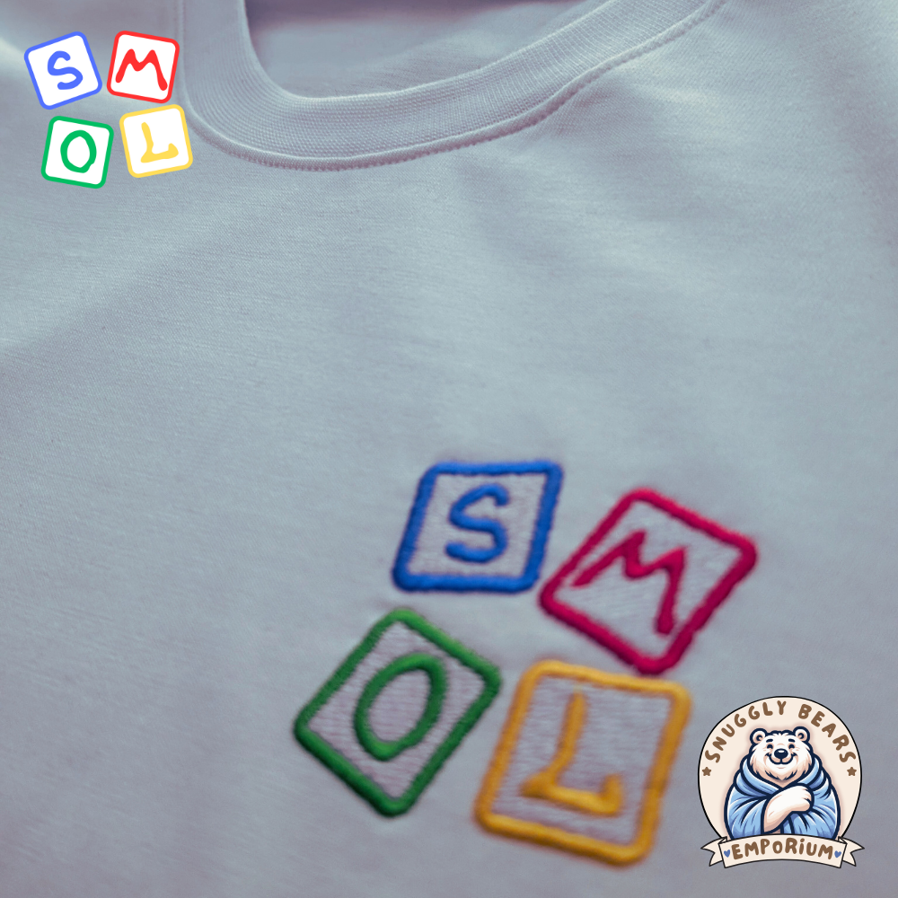 Embroidered SMOL logo in colorful blocks on a soft T-shirt fabric from Snuggly Bears Emporium.